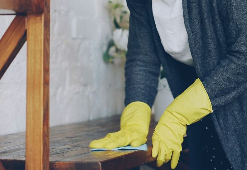 Woman wearing yellow gloves cleaning wooden surface
