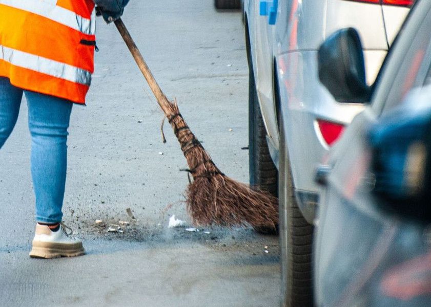 A street cleaner in Tbilisi wearing a reflective vest sweeps debris from the roadside.