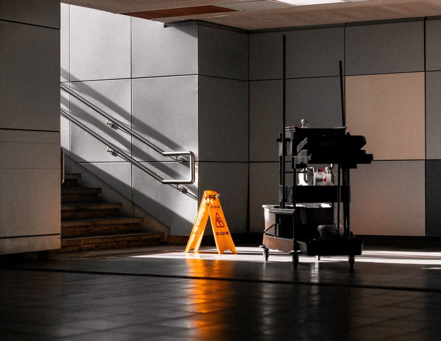 A well-lit underground corridor featuring stairs, cleaning supplies, and warning signs.